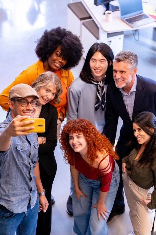 Diverse marketing team taking a group selfie in a bright office, representing collaboration and connection in social-first strategies and digital marketing.