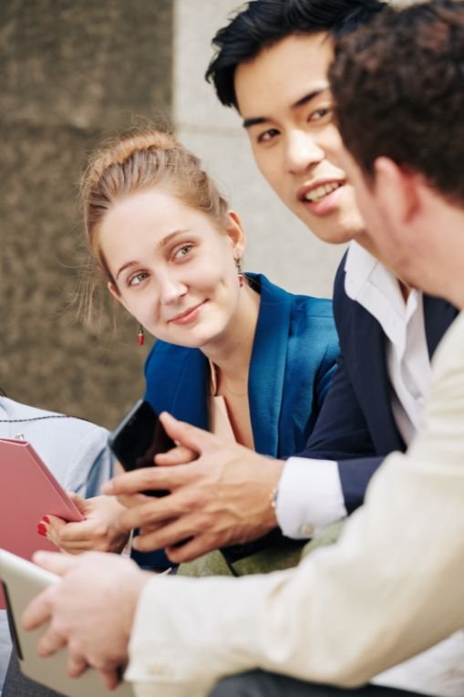 Group of young professionals having a friendly discussion outdoors, using digital tablets and smartphones — concept of collaboration and personalised marketing strategies.