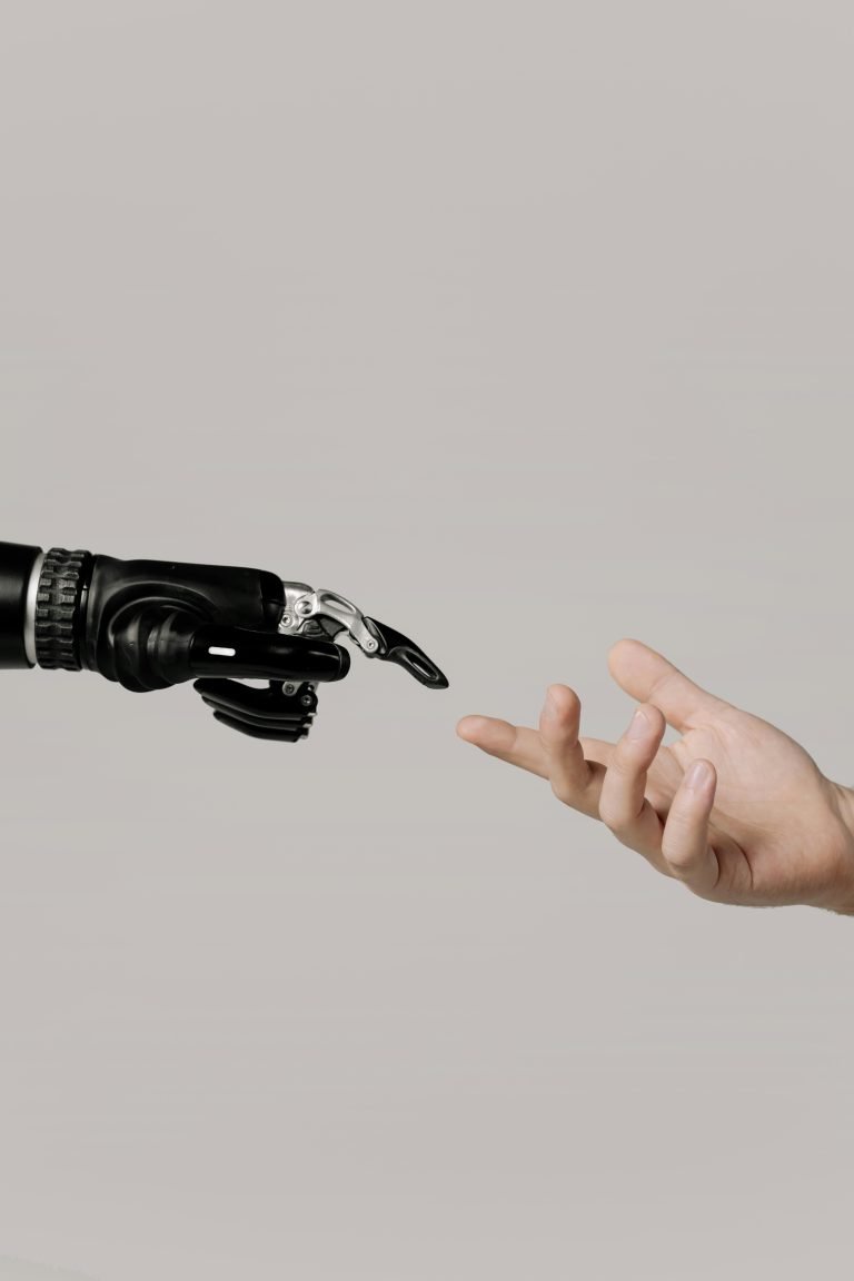 Sora 2 AI video A close-up image showing a human hand reaching out toward a robotic prosthetic hand against a plain neutral background, symbolising the connection between humans and artificial intelligence or technology.